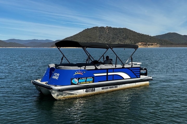 Blue pontoon boat on a lake with mountains in the background, labeled 'For Hire'.