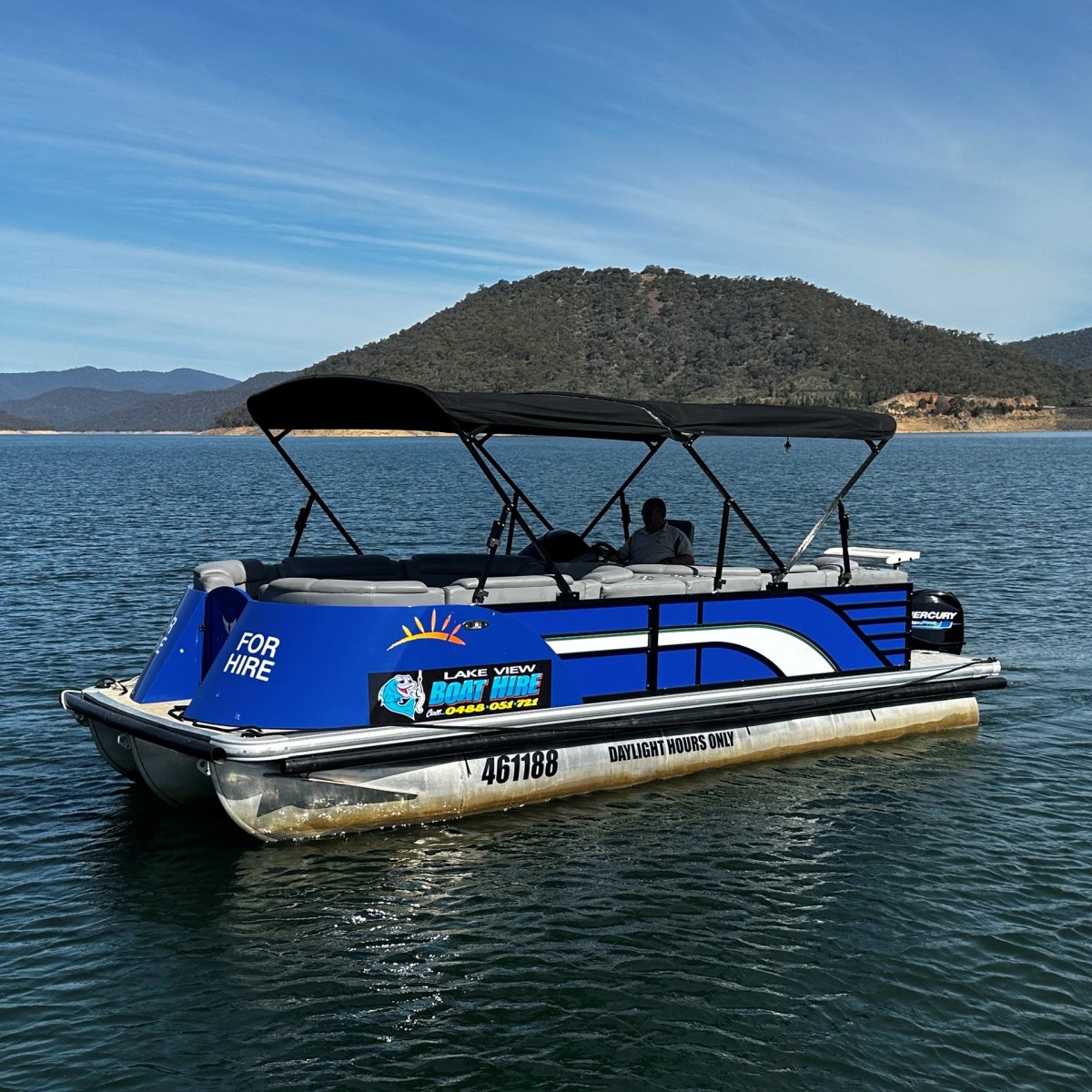 Blue pontoon boat on a lake with mountains in the background, labeled 'For Hire'.