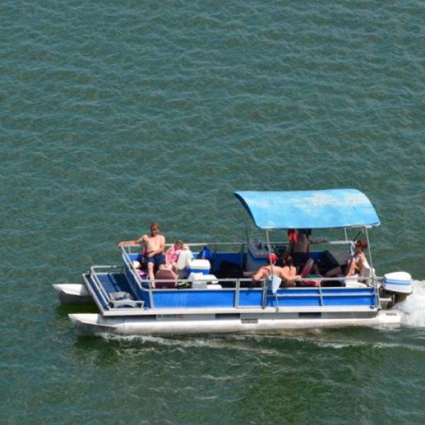 Small boat with canopy and people on lake, moving forward.