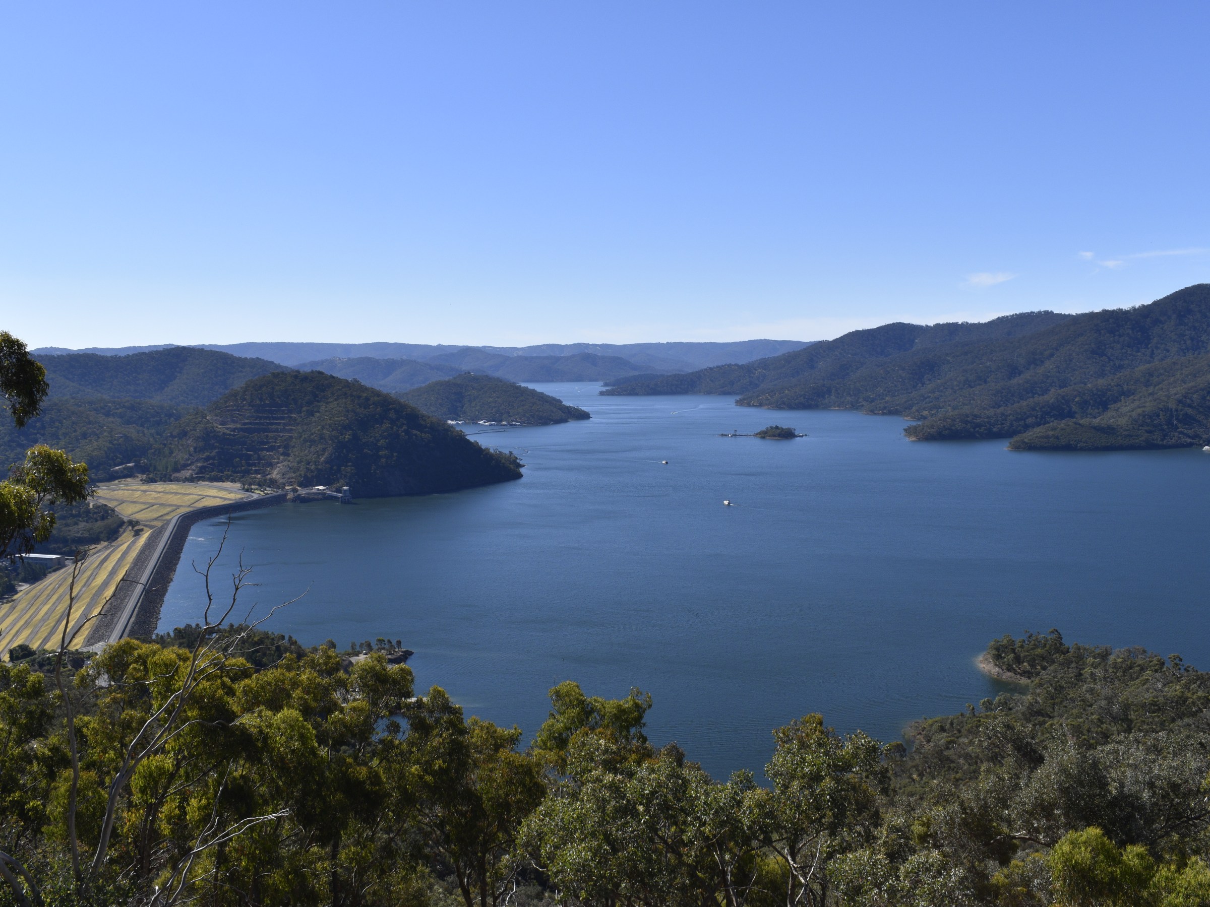 Wide river with forested hills and a clear blue sky in the background.