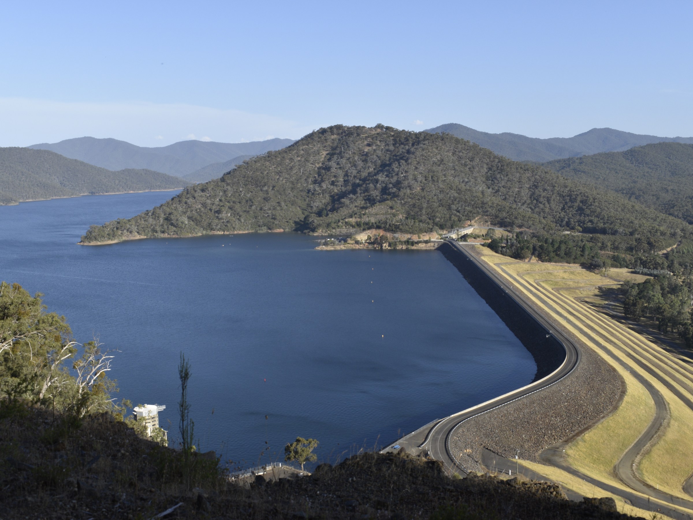 View of a large reservoir, dam, and surrounding hills on a clear day.