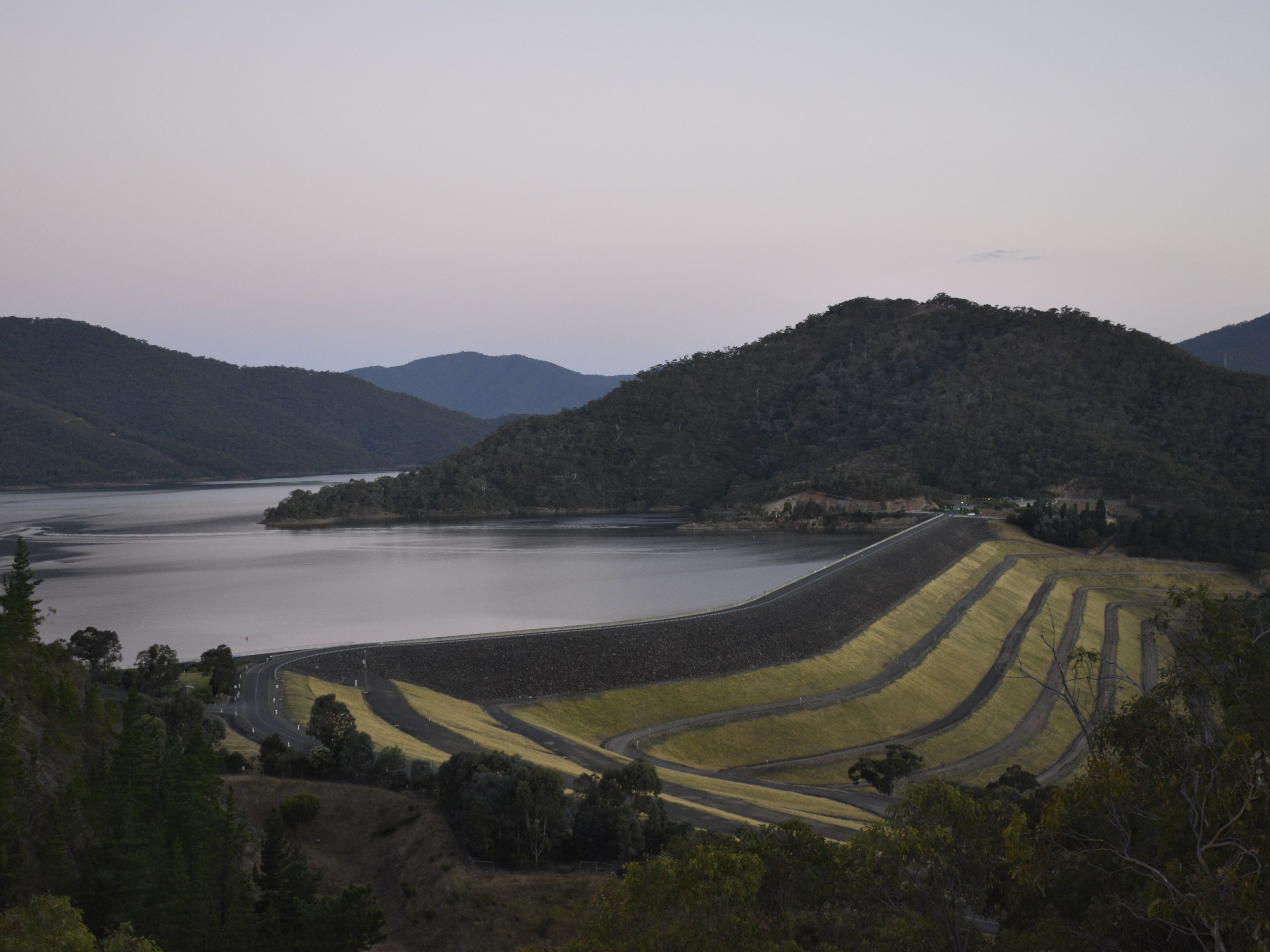 Hilly landscape with a dam and serene lake at sunset.