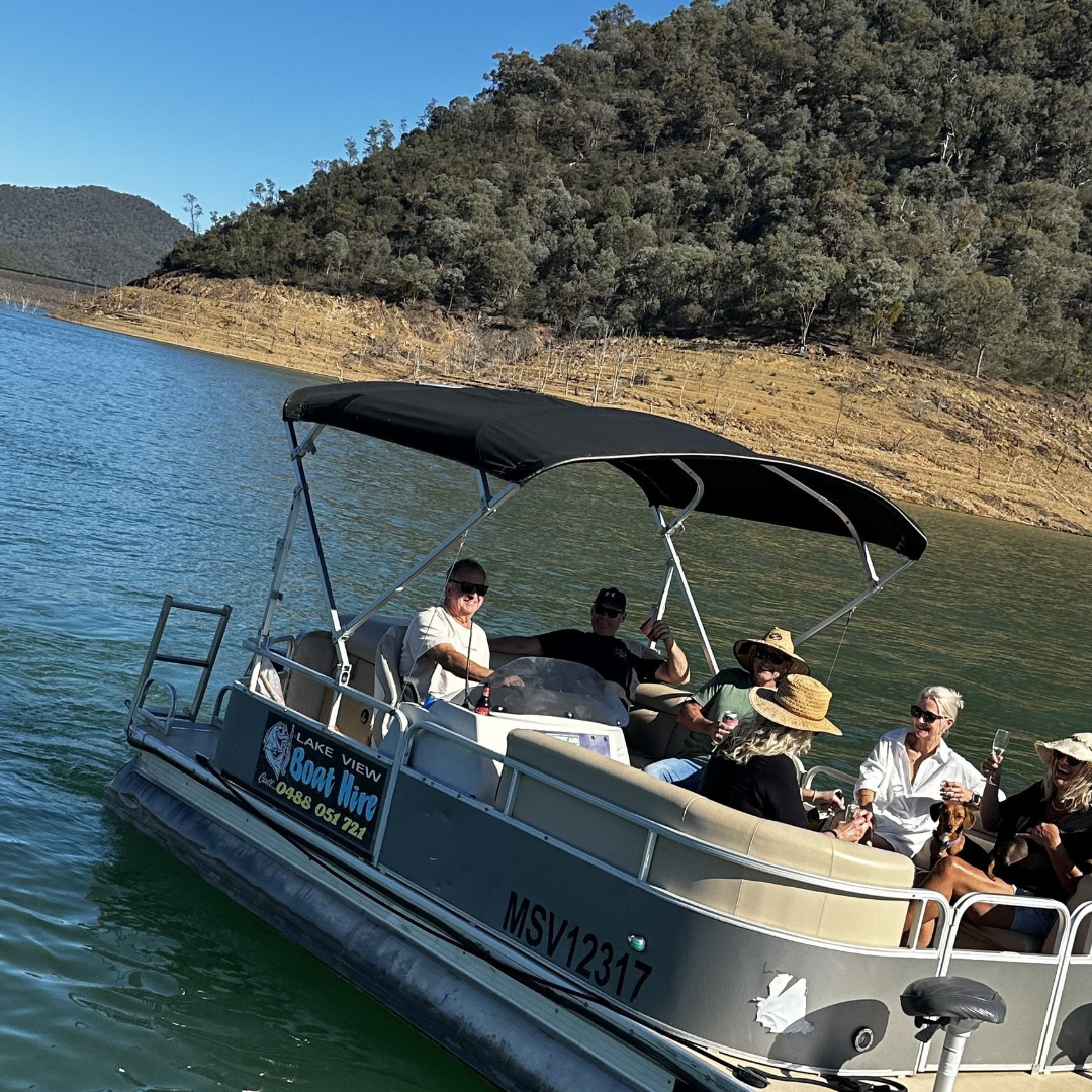 Group on a pontoon boat on a scenic lake with forested hills.