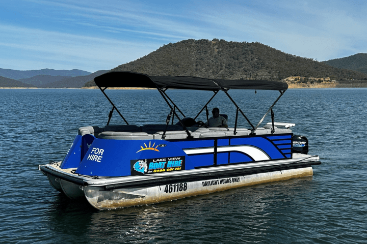 Blue pontoon boat on a lake with mountains in the background.