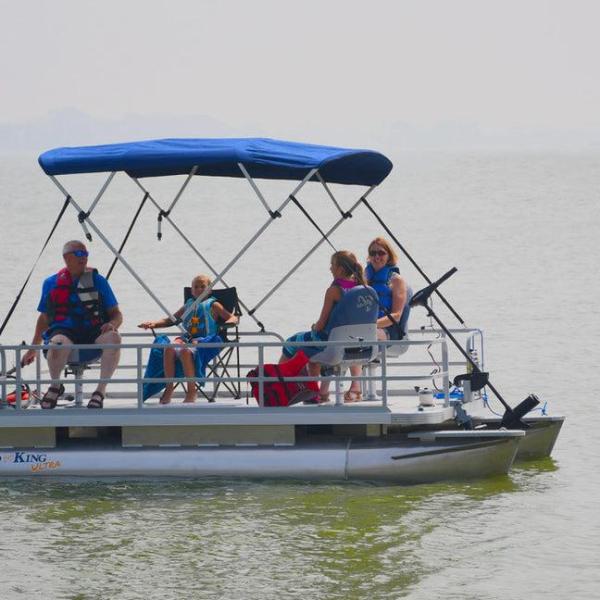 A family on a small pontoon boat with a blue canopy on a lake.