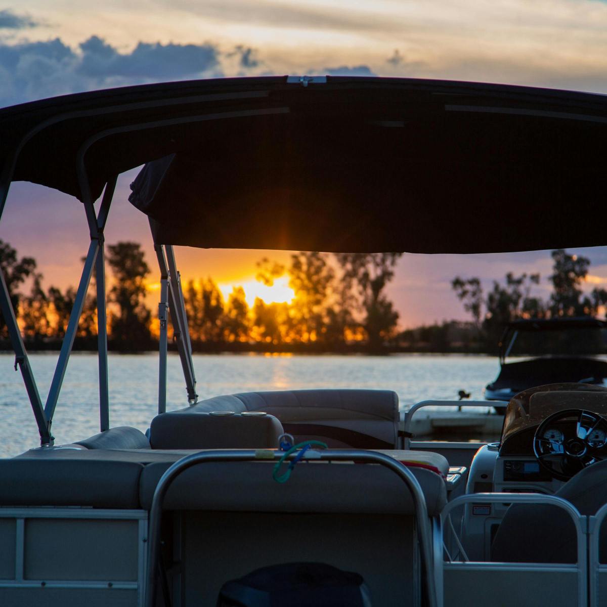 Pontoon boat on lake at sunset with trees silhouetted in background.
