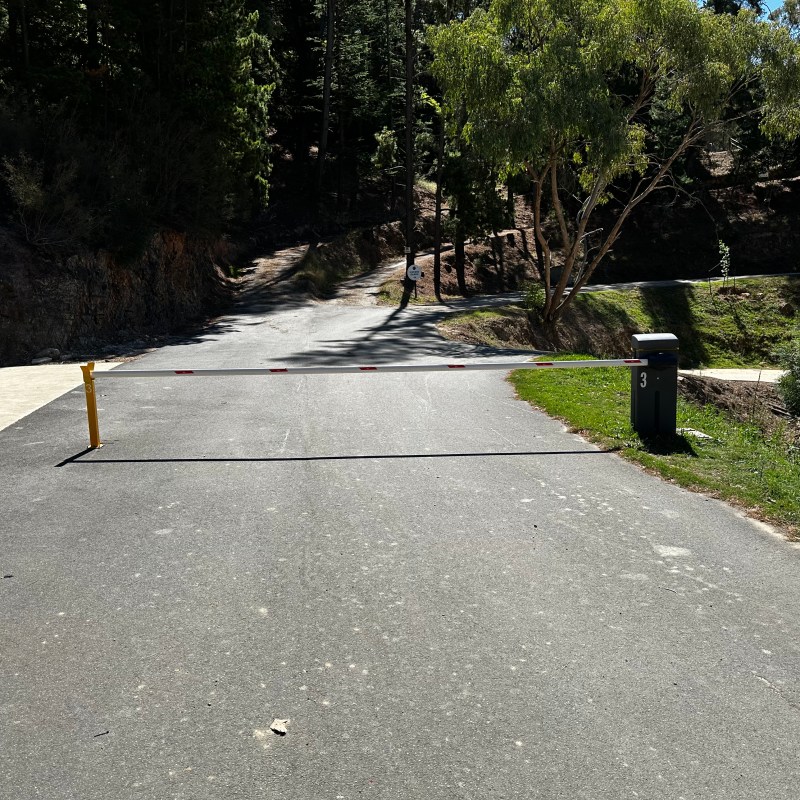 A closed boom gate blocking a paved road surrounded by trees.